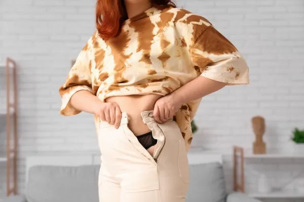 Image of woman trying to do her trousers up after pregnancy weight gain Kington